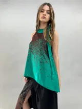 Blusa de satén con escote halter y cuello elevado anudado lateralmente. Presenta un diseño estampado degradado en tonos verde esmeralda y azul, con corte holgado y caída fluida.