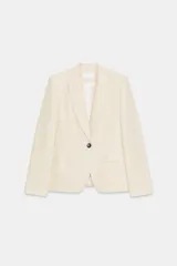 Blazer color crema de lino con cuello solapa y manga larga. Tiene bolsillos de vivo con solapa y cierre frontal con botón.