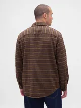 Camisa de manga larga confeccionada en tela de franela con estampado de cuadros en tonos azul claro, blanco y negro. Presenta cuello clásico, cierre frontal con botones y un bolsillo en el pecho.