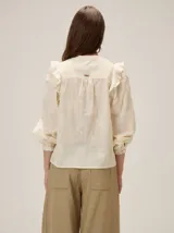 Camisa de color crema con bordados florales, cuello mao, cierre frontal con botones y mangas largas abullonadas con volados en los hombros.