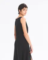 Vestido largo negro sin mangas, con cuello redondo, corte holgado y abertura lateral en la falda. Presenta un cinturón con hebilla metálica plateada.