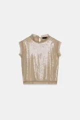 Top color tostado decorado con lentejuelas en el frente, cuello redondo y mangas sisa con detalles semitransparentes en cuello y sisas. Cuenta con cierre en la espalda con abertura y lazada.