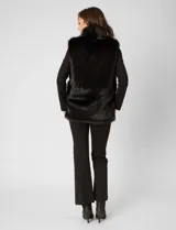 Chaleco de piel sintética Adrienne Landau, color negro, con cuello alto envolvente, cierre frontal con broche oculto y bolsillos laterales funcionales.