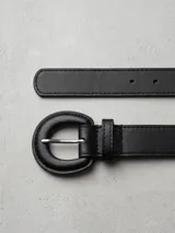 Cinturón de cuero sintético negro con hebilla redonda forrada en el mismo material y herraje metálico plateado.