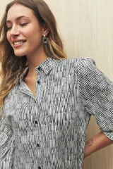 Camisa blanca con estampado lineal irregular en negro, de calce relajado, cuello clásico, abotonadura frontal y mangas largas con puños elastizados.