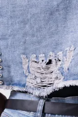 Campera de jean cropped con tachas plateadas distribuidas en el frente, hombros y mangas. Presenta un diseño con bordes deshilachados, cuello clásico y cierre frontal con botones metálicos.