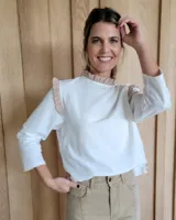 Blusa blanca de manga larga con cuello alto y volados en cuello y hombros.