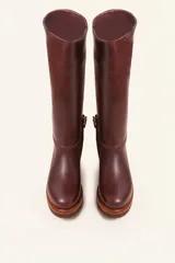 Bota de caña alta confeccionada en cuero vacuno suave, con diseño minimalista y suela de goma robusta. Presenta costuras visibles en la zona del empeine y un taco bajo cuadrado.