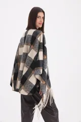 Mantela de tejido de punto con diseño de cuadros grandes en tonos negro, gris y beige. Presenta un cierre frontal con trabilla y terminaciones con flecos en el ruedo.
