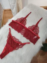 Conjunto de lencería de dos piezas confeccionado en encaje rojo. Incluye un bralette estilo top con breteles regulables y una tanga con laterales ajustables.