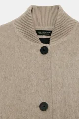 Cazadora bomber beige confeccionada en hilatura con lana, con cuello subido, manga larga y bolsillos frontales. Presenta cierre frontal con botones oscuros y puños, cuello y ruedo en tejido rib.