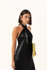 Vestido midi de satén color negro, con escote halter cruzado y ruedo terminado en flecos largos.