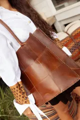 Bolso tote grande de cuero natural en color marrón, con diseño de piezas unidas mediante costuras visibles y asas de hombro.