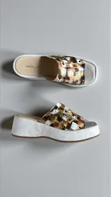 Sandalias de plataforma con capellada de cuero natural pintada a mano con un diseño abstracto en tonos neutros, dorados y terracota, con base y plantilla acolchonada de color blanco.