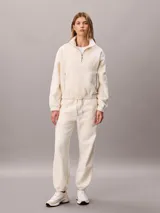 Jogger de tejido polar color blanco de Calvin Klein, con cintura elástica con cordón ajustable, bolsillos laterales con cremallera y puños elásticos en los tobillos.