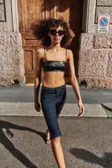 Jeans de tiro medio en denim azul oscuro, con diseño capri de pernera entallada. Presenta cierre frontal con cremallera y botón, y un cinturón integrado con hebilla metálica en la cintura.