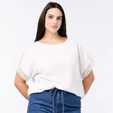 Camiseta blanca de manga corta holgada, con detalles de bordado y macramé en las mangas y cuello redondo.