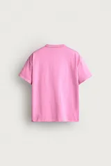 Camiseta cropped de corte relajado, color beige, con cuello redondo y mangas cortas. Cuenta con un estampado frontal con texto en tonos rosados y detalles de efecto desgastado en el cuello.