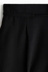 Pantalón de tiro alto con piernas amplias, pinzas frontales y raya marcada. Cuenta con cierre oculto, cordón ajustable en la cintura, bolsillos laterales discretos y bolsillos traseros insertados.