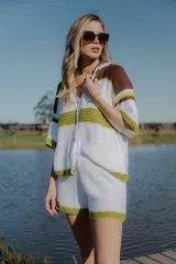 Conjunto tejido de algodón color blanco con rayas horizontales en marrón y verde. Incluye camisa de manga corta con cuello polo y cierre frontal con botones, y short de tiro alto con cintura elástica.