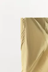 Falda midi de tiro medio confeccionada en tejido satinado color beige. Presenta un diseño asimétrico con costuras marcadas y aplicación de encaje a tono en el bajo. Cuenta con cierre lateral oculto.