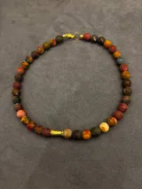 Collar corto de piedras volcánicas marrones y marrones oscuras, con detalle cilíndrico dorado en el centro.