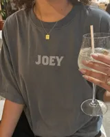 Remera oversize gris oscuro con corte holgado, mangas cortas y estampa trasera en blanco y negro con forma de estampilla que muestra a una persona con un gato y el texto 'Kaboa Industries'.