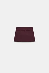 Falda pantalón de tiro medio en color bordó, con diseño cruzado en el frente y detalle de cinturón fino integrado con hebilla metálica.
