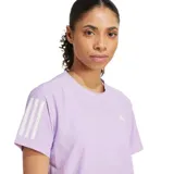 Remera deportiva Adidas Own The Run de mujer, color lila claro, con cuello redondo y manga corta. Presenta las tres franjas blancas en ambas mangas y el logo Adidas Badge of Sport en blanco en el pecho. El cuello tiene una cinta interior con texto repetido.
