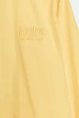 Camisa de popelín color amarillo de Fruit of the Loom x Zara, con cuello solapa, manga larga, puños anchos y cierre frontal con botones. Cuenta con un delicado bordado a tono en el delantero.