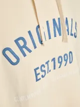 Canguro oversize color blanco roto con capucha y cordones ajustables. Presenta un estampado frontal en azul con la palabra "ORIGINALS" y "EST.1990", y texto más pequeño "CONTEMPORARY EDIT. DESIGNED IN COPENHAGEN". Tiene bolsillo canguro y puños y dobladillo acanalados.