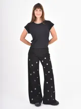 Jean de corte recto y tiro alto, color negro, con diseño de ojales metálicos distribuidos por toda la prenda.