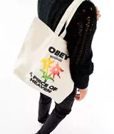 Bolso tipo tote bag color crudo, con asas de algodón y estampado con el logo de Obey, flores y la frase "A Piece of Heaven".