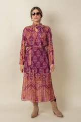 Vestido midi plisado de gasa estampada en tonos violeta y naranja, con lazo en el cuello y en la cintura.