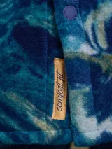Sobrecamisa de tejido polar con estampado abstracto en tonos rojizos y azul marino. Presenta cuello clásico, cierre frontal con botones a presión, dos bolsillos frontales con solapa en el pecho y un parche decorativo.