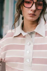 Remera tipo polo de tejido de punto a rayas horizontales en tonos rosados y beige. Presenta cuello camisero de lino, cierre frontal con botones de nácar y silueta holgada.