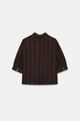 Blusa blanca de cuello alto con detalles de puntilla, manga corta abullonada y cierre posterior con botón.
