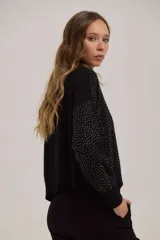 Sweater de punto negro con cuello alto y diseño de puntos brillantes en contraste. Presenta mangas largas con puños ajustados y un corte recto a la cintura.