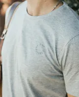 Remera de manga corta, cuello redondo, color gris jaspeado, con un pequeño logo circular estampado en el pecho.