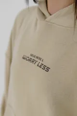 Canguro negro con capucha y bolsillo delantero tipo canguro. Estampa frontal con la frase "Wear More & Worry Less" en color rosa.