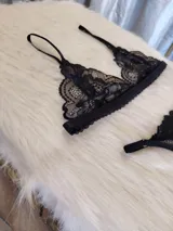 Conjunto de lencería compuesto por un bralette de encaje con breteles regulables y una tanga regulable con corte cola less. Ambas piezas presentan un diseño de encaje floral negro.