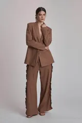Blazer marrón con solapas de muesca, cierre frontal con lazo y mangas largas. Presenta volados a lo largo de las costuras laterales del pantalón a juego.