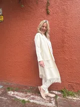 Saco largo crudo con solapa, delicados flecos en el ruedo y bolsillos plaqué delanteros.