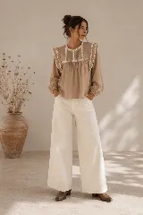 Blusa color tostado con cuello redondo, mangas largas abullonadas con puños elastizados, y detalles de puntillas y bordados en el frente y hombros.