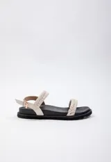 Sandalia baja color crema con doble tira trenzada en el empeine y tira de agarre en el tobillo con hebilla dorada. Cuenta con plataforma de 3 cm de alto y suela negra.
