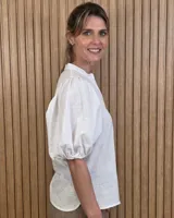 Camisa de algodón a rayas color beige y blanco, con escote en V, cuello mao y mangas cortas abullonadas. Cuenta con cierre frontal de botones oscuros.
