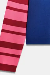 Chaqueta de punto con cuello redondo y manga larga. Presenta un diseño color block con el pecho en rojo, la parte inferior en azul y mangas a rayas horizontales en rosa y rojo. Cierre frontal con botones.
