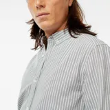 Camisa de corte clásico confeccionada en tejido Oxford, con diseño de rayas verticales en tonos verde y blanco. Presenta cuello abotonado, cierre frontal con botones y mangas largas con puños abotonados.