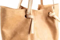 Bolso tipo tote de cuero negro con acabado brillante, diseño fruncido en los laterales y correas de hombro de tela tejida en tono beige.