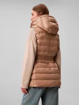 Chaleco puffer acolchado color tostado de la marca Calvin Klein, con diseño sin mangas, cuello alto y capucha desmontable. Cuenta con cierre frontal de cremallera y un cinturón elástico ajustable con hebilla de clip con el logo de la marca.